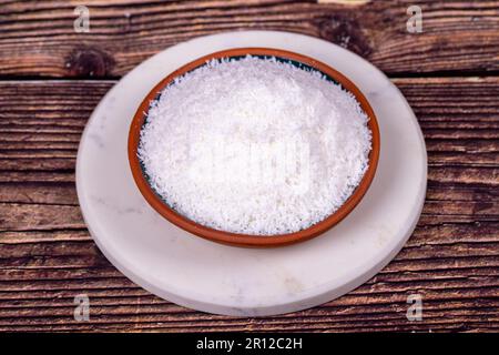 Grounded coconut flakes on wooden background. Coconut shavings in clay bowl Stock Photo