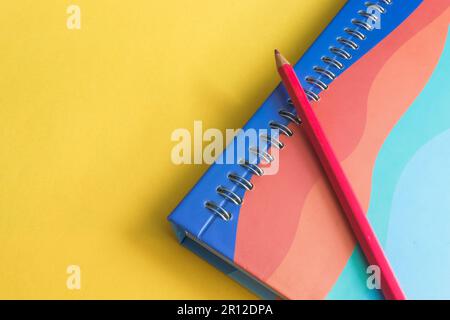 A white spiral notebook lies on a bright yellow background, with a red pencil on it Stock Photo