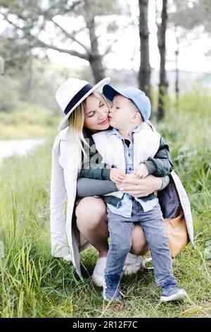 Pregnant woman with kid outdoors. Mother and her son on nature in spring forest. Little child boy kissing mother, who pregnant for second time Stock Photo