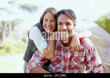 Excited to start their tent. A young couple smiling at the camera in front of a camping tent. Stock Photo