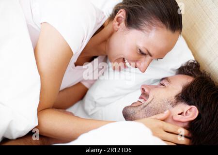 Come here you. a young couple playfully embracing in bed. Stock Photo