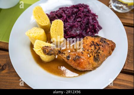 Baked chicken thigh, stewed red cabbage and sliced fluffy potato dumpling on white plate, closeup. Stock Photo