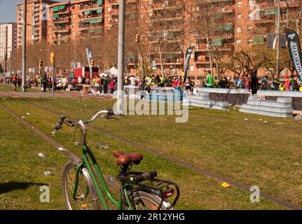 A green step through bicycle beside discarded plastic bottles in the foreground of people running the Barcelona Marathon on the urban streets on a hot Stock Photo
