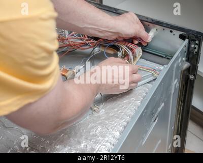 Serviceman locating faulty parts in the broken electric oven Stock Photo