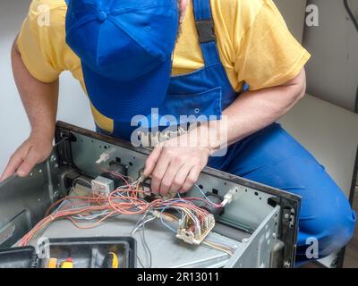 Serviceman replacing faulty thermostat in the broken electric oven Stock Photo