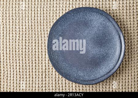An empty dark blue ceramic plate against the background of a beige knitted sweater. Top view with copy space Stock Photo