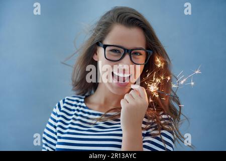 Everyday Im sparklin. Studio shot of a beautiful young woman holding sparklers against a blue background. Stock Photo