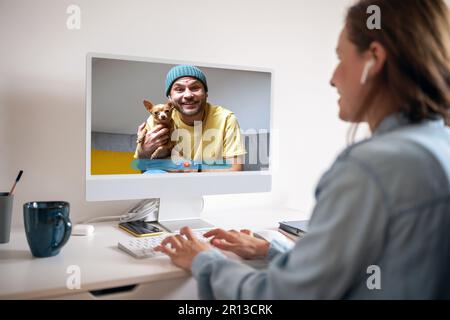 Young couple with dog have online meeting on the internet using computer. Stock Photo