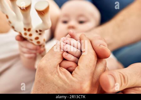 Close-up of the hands of parents holding their child's tiny hand. Mom and dad hold the hand of a newborn little son or daughter, playing, touching the Stock Photo