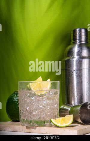 Cold iced Ti punch alcohol cocktail, small punch, rum-based mixed drink with fresh lime slice garnish, on high-colored green background Stock Photo