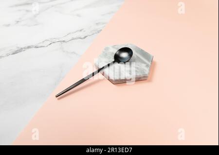 Black dessert spoon on marble background. White marble and pink background. Black cutlery, copy space. Stock Photo