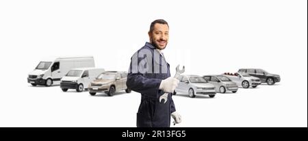 Auto mechanic holding a wrench and standing in front of parked vans and cars isolated on white background Stock Photo