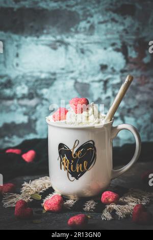 Mug with heart print and text be mine, filled with coffee or cocoa with whipped cream and pink chocolate hearts, rustic background, copy space Stock Photo