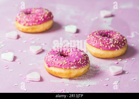 Donuts, Berliner, Krapfen with pink sugar icing on pink textured background, decorated with pink and white sugar and paper hearts Stock Photo