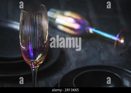 Pink shimmering champagne glass and black stoneware on a rustic black table, one glass lying in the background Stock Photo