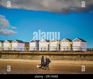 Dog walkers in winter in front of the locked up beach huts on St Annes seafront Stock Photo