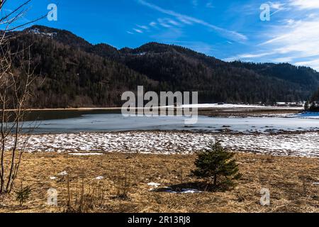 Alpine landscape with a frozen lake at the end of winter, partly covered with snow Stock Photo