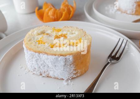 Swiss roll or biscuit roll with whipped cream and mandarin filling sliced on a plate Stock Photo