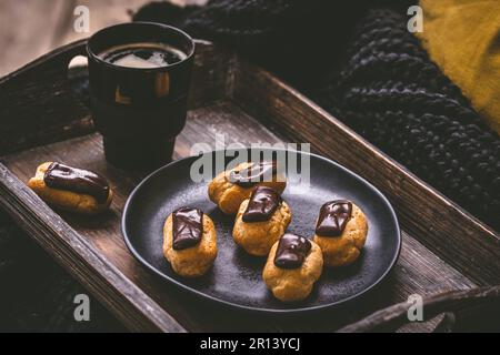 Mini eclairs with dark chocolate and a coffee on a wooden tray, french pastry specialty with custard cream Stock Photo
