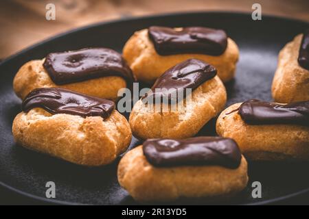 Mini eclairs with dark chocolate on a black plate, french pastry specialty with custard cream Stock Photo