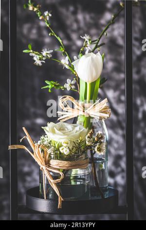 Spring decoration with white rose and tulip in a modern black metal stand, gray background, vertical Stock Photo