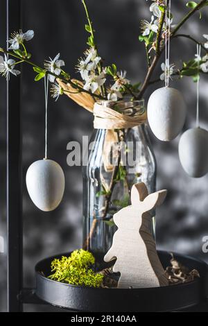 Easter decoration with white cherry blossom branches and white eggs in a black metal stand, gray background, vertical Stock Photo