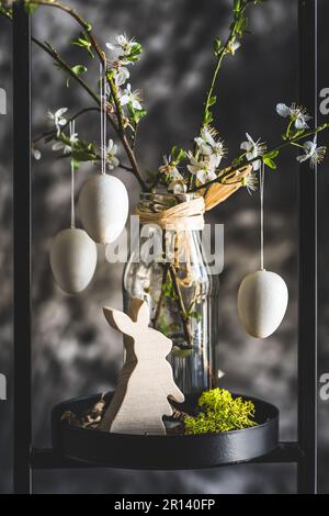 Easter decoration with white cherry blossom branches and white eggs in a black metal stand, gray background, vertical Stock Photo
