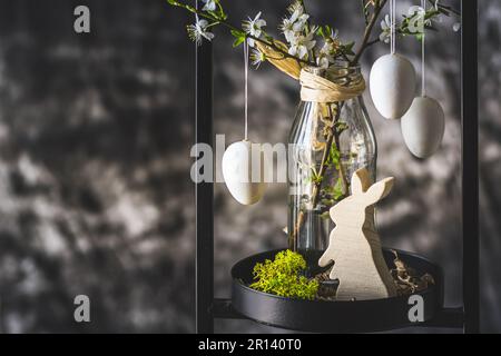 Easter decoration with white cherry blossom branches and white eggs in a black metal stand, gray background, copy space Stock Photo
