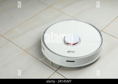 Robotic vacuum cleaner on white tiled floor Stock Photo