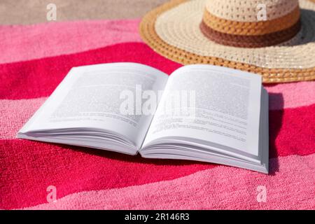 Open book, hat and striped towel on sandy beach Stock Photo