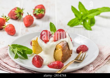 Piece of homemade cheesecake with whipped cream and fresh strawberries on white wooden background, decorated with fresh mint leaves Stock Photo