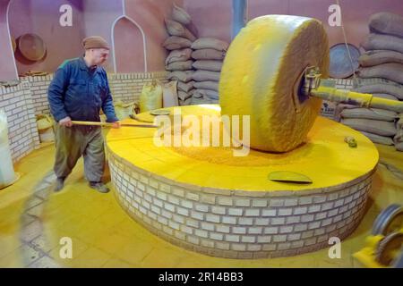 A worker in a mill in the old town of Kashan, Iran. A big millstone or grindstone for grinding and pressing. Stock Photo