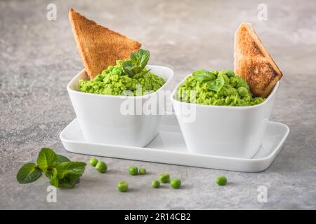 Two bowls of pea puree with basil, mint and roasted bread on rustic gray background Stock Photo