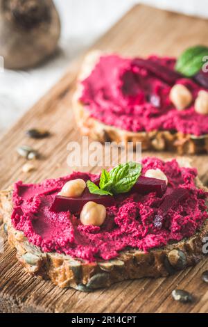 Wooden board of bread slices with beetroot hummus on a white wooden background, vertical Stock Photo