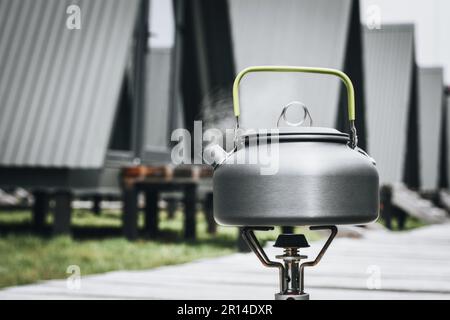 Cooking, heating a tourist kettle on a portable gas burner with a red gas cylinder. Cooking in a tourist campsite in the mountains. Summer outdoor Stock Photo