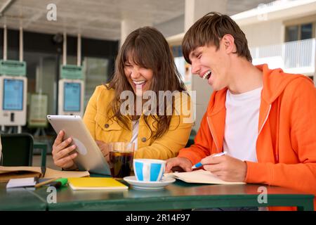Laughing creative male and female students searching useful web pages using tablet. Stock Photo
