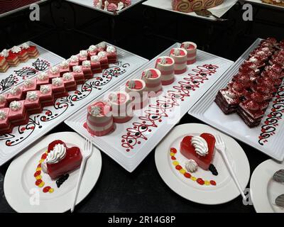 Showcase with sweets. Colored сakes on white plates on black table. Stock Photo