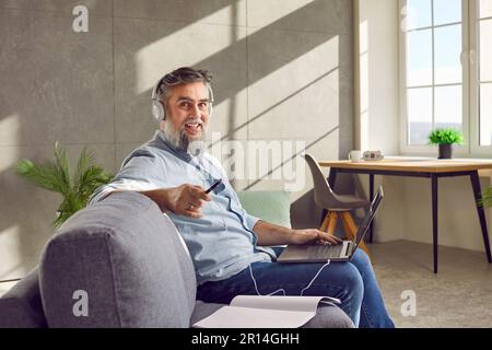 Middle aged man in headphones using laptop at home Stock Photo