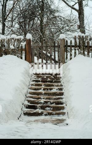 Stone steps with snowdrifts on the edges leading to a wooden gate in the fence. Stock Photo
