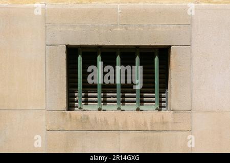 Small rectangular window on a stone wall, covered with green metal bars. From the Window of the World series. Stock Photo