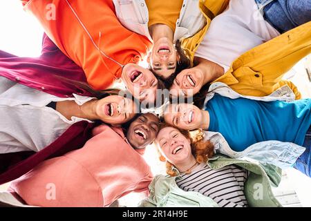 Large multiracial group of smiling young people standing hugging looking at camera. Low angle view. Stock Photo