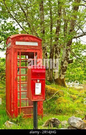 Old and rusted red telephone booth and post box on a pole at the coast of the scottish Highlands. Stock Photo