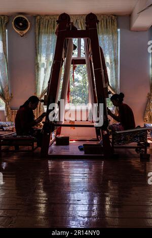 two young ladies in silhouette working on upright loom to hand weave silk carpet in factory in samarkand uzbekistan Stock Photo