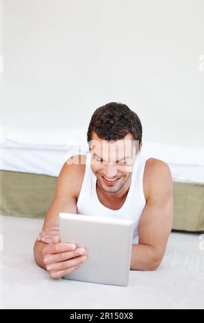 Enjoying touchscreen technology. A handsome man lying on his bed working on his digital tablet. Stock Photo