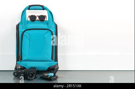 Travel bag with sunglasses, camera, wallet, and keys against a white wall. Ready for a vacation holiday. Stock Photo
