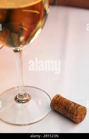 Glass of white wine and cork on white linen table Stock Photo