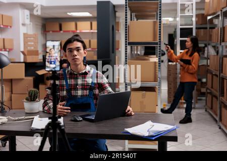 Retail storehouse employee taking goods marketing video on smartphone at storage room desk. Logistics and distribution manager explaining supply chain process on mobile phone camera Stock Photo