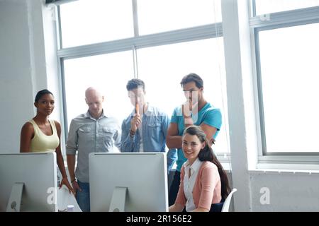Problem solving is their pleasure. A group of designers standing in a office together around a computer screen to run over their plans. Stock Photo