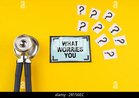 Medical concept. Question. On a yellow background a stethoscope, question marks and a blue sticker with the inscription - What worries you Stock Photo