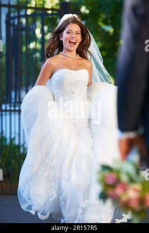 She cant get to him fast enough. Fun full length shot of a new bride running happily through church grounds. Stock Photo